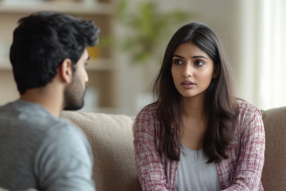 Indian woman calming upset offended guy support and caring sitting on sofa at home free space Sorry after quarrel relationship problems bad news