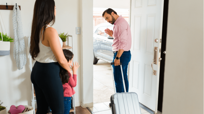 a man walking out the door, a woman and a child are standing by and watching him leave
